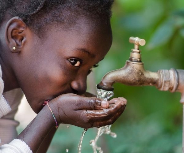 fillette qui boit au robinet en Afrique